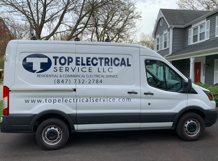 white top electrical van outside of a dark grey house with a grey roofing